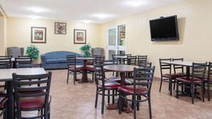 A dining area with multiple tables and chairs, a blue sofa, and a television mounted on the wall. - Days Inn by Wyndham Faribault (Faribault)