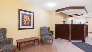 A reception area with a reception desk, two patterned armchairs, a bench, and a framed picture on the wall. - Days Inn by Wyndham Faribault (Faribault)
