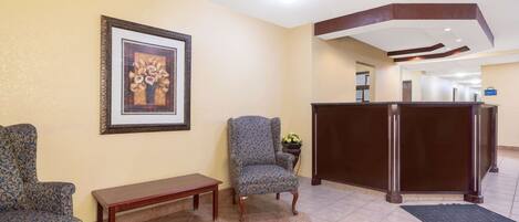A reception area with a reception desk, two patterned armchairs, a bench, and a framed picture on the wall.