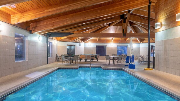 An indoor swimming pool with wooden beams, tiled walls, and seating areas. - Days Inn by Wyndham Faribault (Faribault)