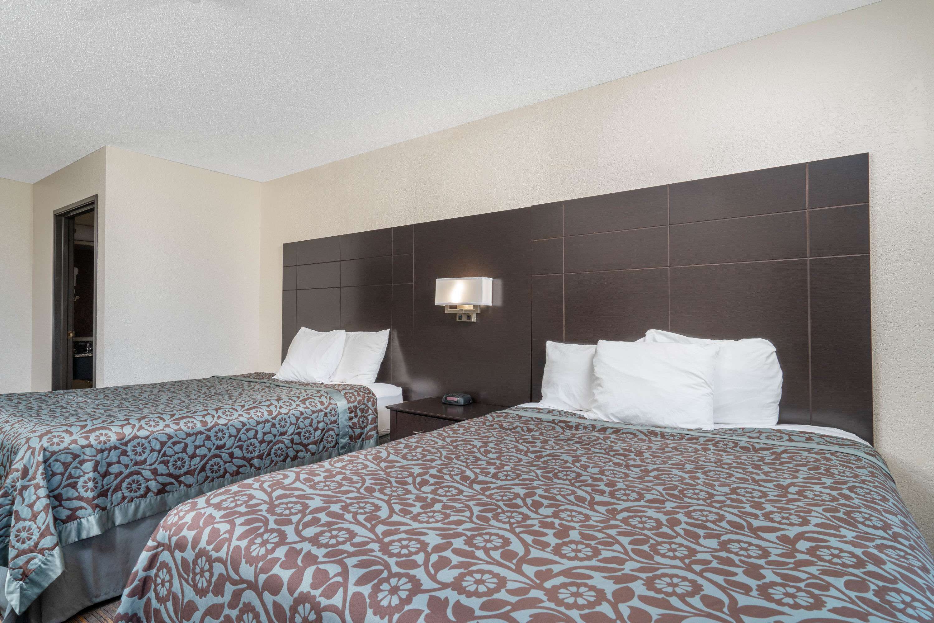 A hotel room with two beds, each with patterned bedding, a nightstand, a wall-mounted lamp, and a door to a closet.