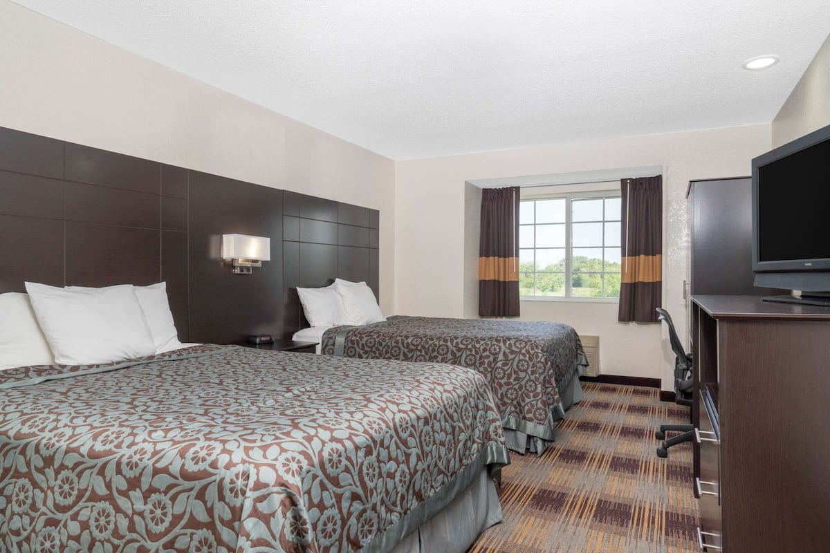 A hotel room with two beds, a TV, a desk, and a window with curtains.