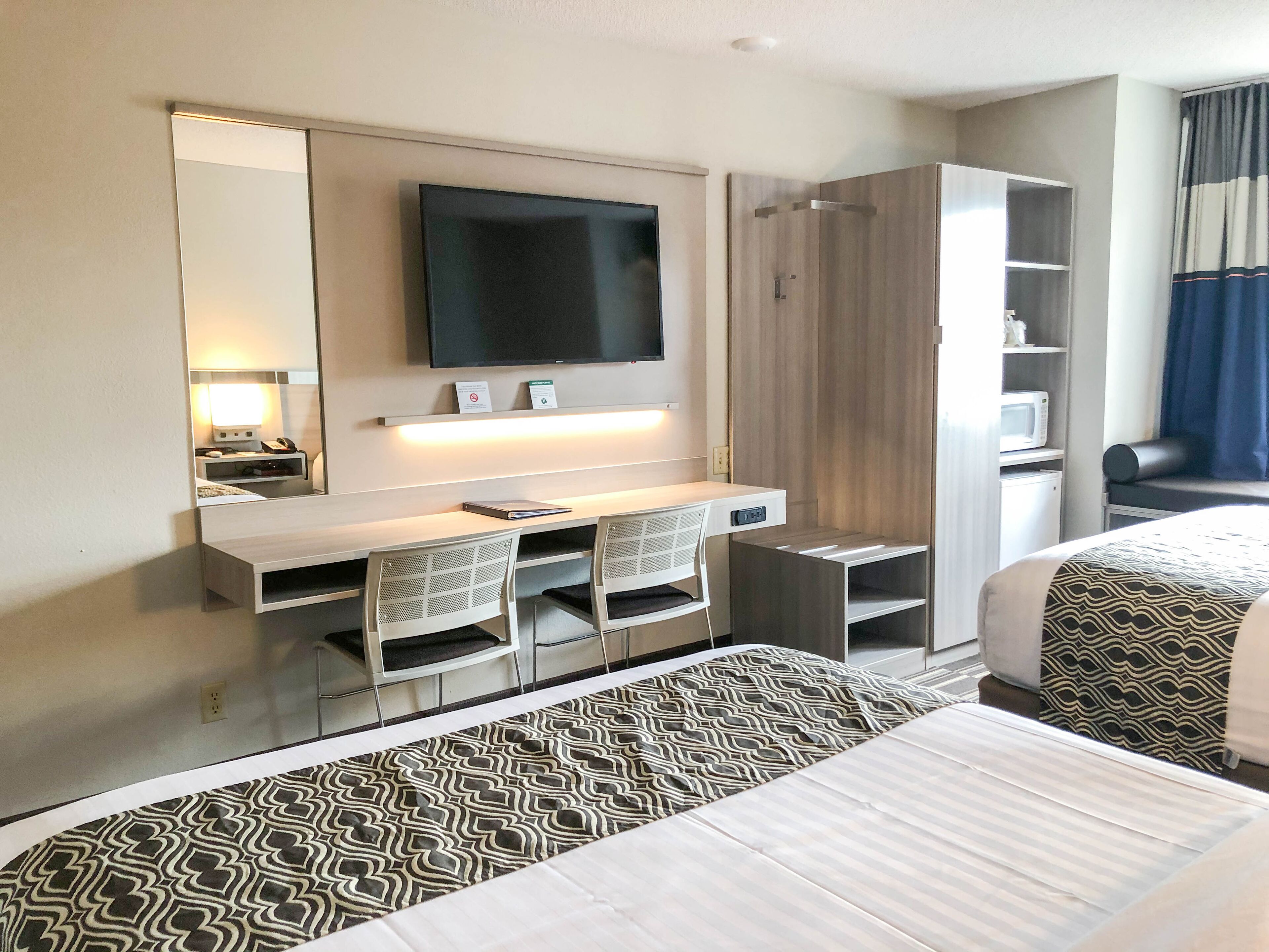 Ein Hotelzimmer mit einem Bett, einem Schreibtisch mit zwei Stühlen, einem an der Wand befestigten Fernseher und einem Kleiderschrank.