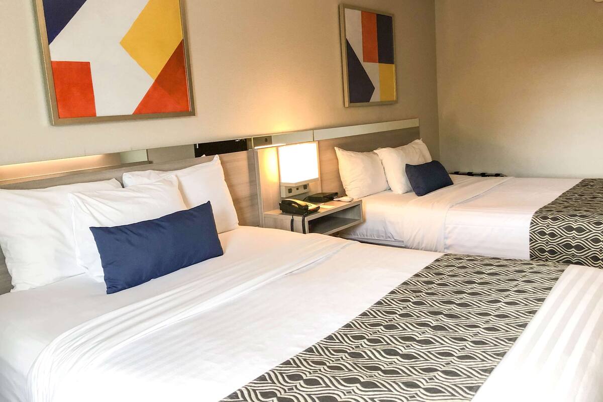 Ein Hotelzimmer mit zwei Betten, einem Nachttisch mit Lampe und abstrakten Wandbildern.