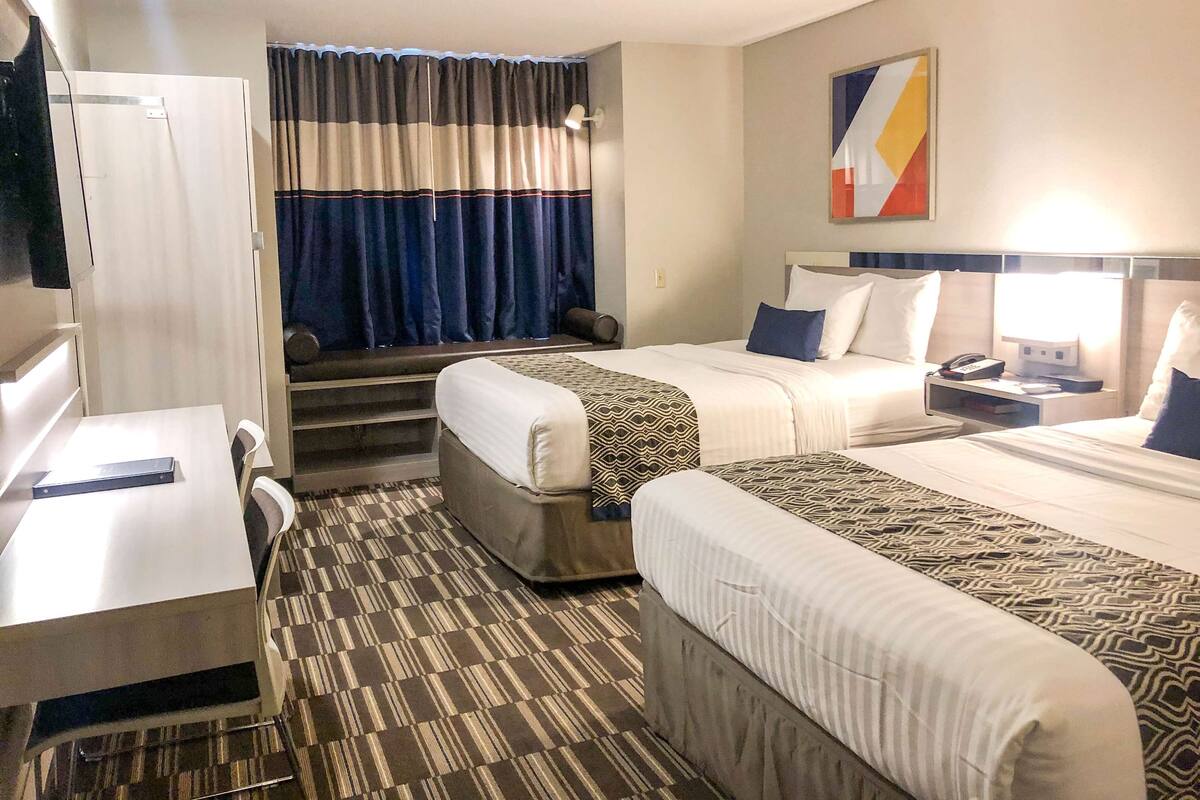 Ein Hotelzimmer mit zwei Betten, einem Schreibtisch, einem Stuhl, einem Fernseher und einem Fenster mit Vorhängen.