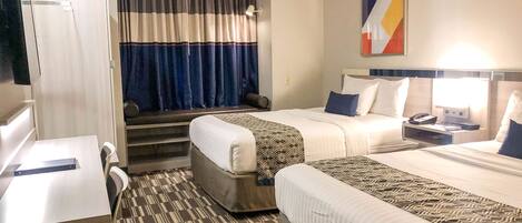 A hotel room with two beds, a desk, a chair, a TV, and a window with curtains.