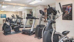 Un gimnasio con varias máquinas de cardio, incluyendo cintas de correr y elípticas, dispuesto en un espacio amplio con un espejo grande y un cuadro en la pared.