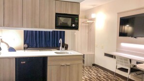 Cocina compacta con microondas, lavabo y televisor de pantalla plana.