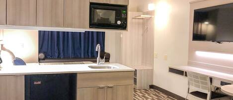 A compact kitchen with a microwave, sink, and a flat-screen TV.