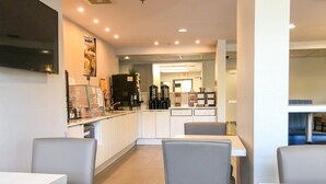 Un café moderno con mostrador, zona de mesas y una cocina a la vista.