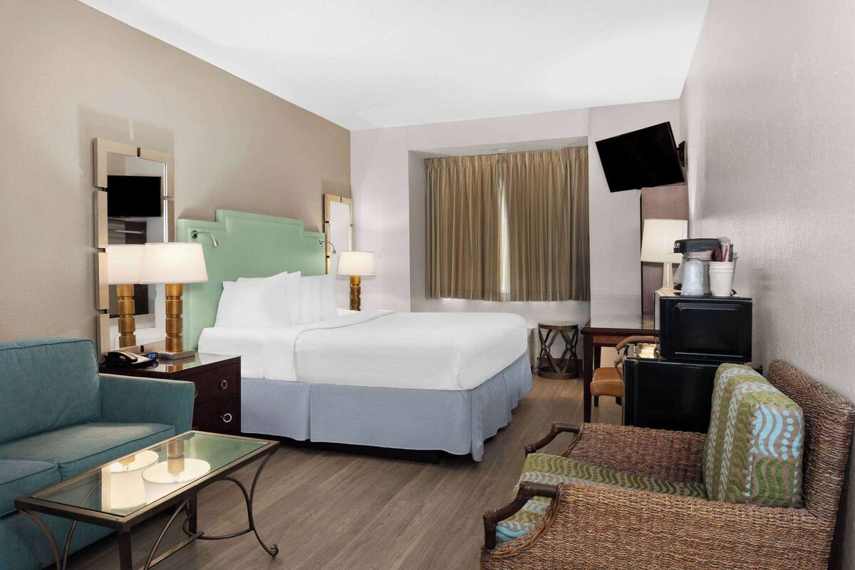 A hotel room with a bed, a sofa, a small table, a TV, and a desk with a chair.
