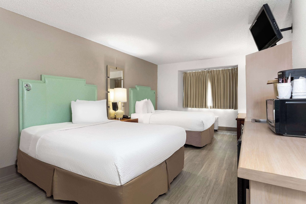 A hotel room with two beds, a TV, a desk with a coffee maker, and a window with curtains.