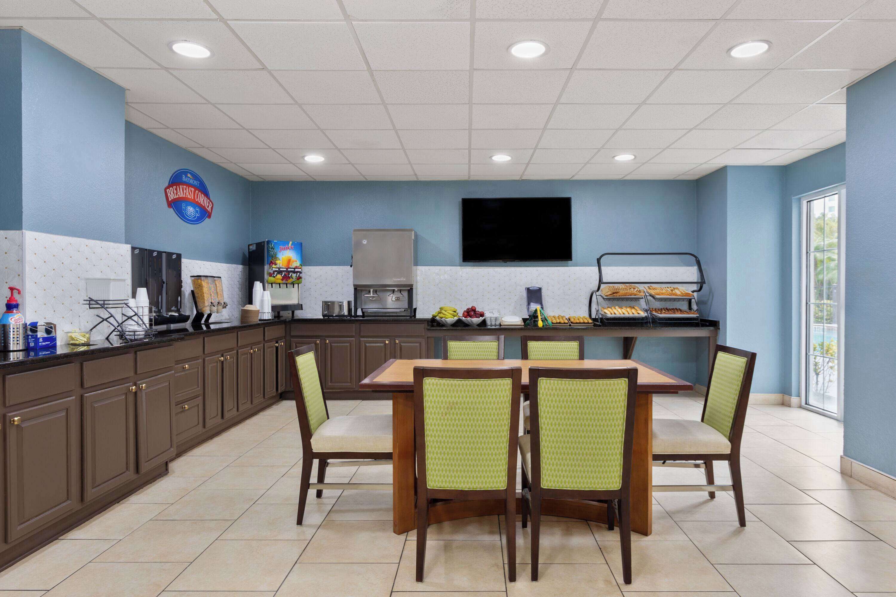 Un restaurante con barra de desayuno, un televisor en la pared y un ventanal que proporciona luz natural.