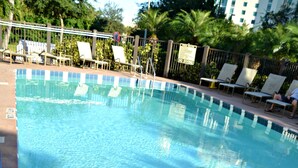Piscina con barandilla de metal, rodeada de sillas de descanso y una valla.