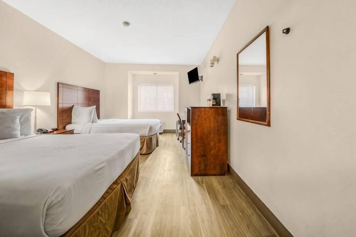 A hotel room with two beds, a wooden dresser, a TV, and a window.