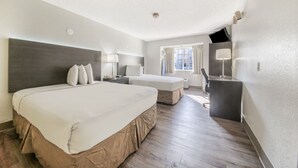 Habitación de hotel con dos camas, un escritorio, un televisor y una ventana con cortinas.