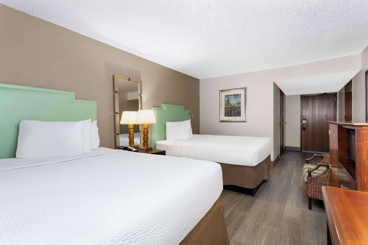 A hotel room with two beds, a nightstand with a lamp, a wooden dresser, and a framed picture on the wall.