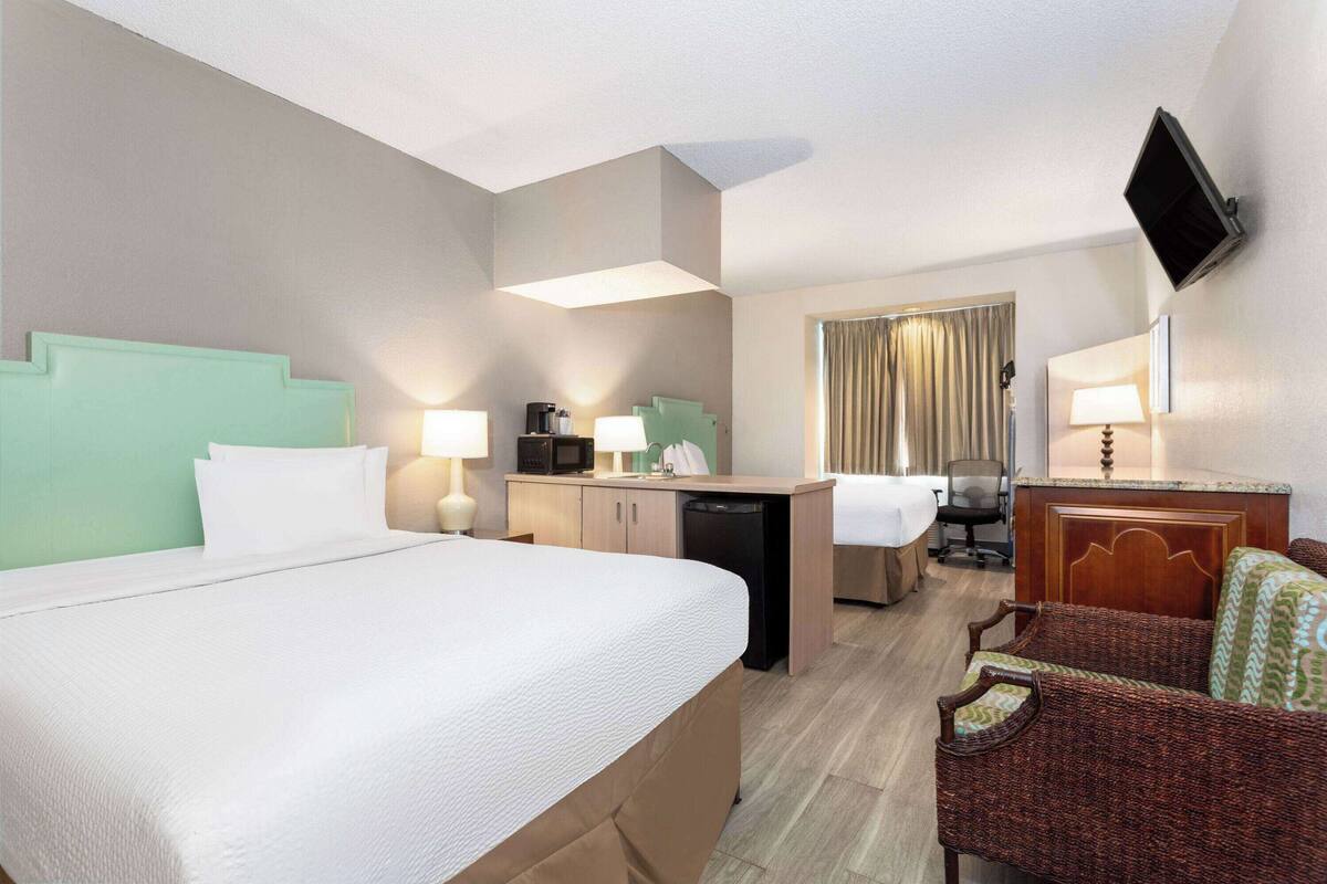 A hotel room with a large bed, a desk with a computer, a microwave, and a television mounted on the wall.