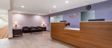 Zona de recepción de un hotel con un mostrador de madera, dos sofás de cuero y un reloj en la pared.