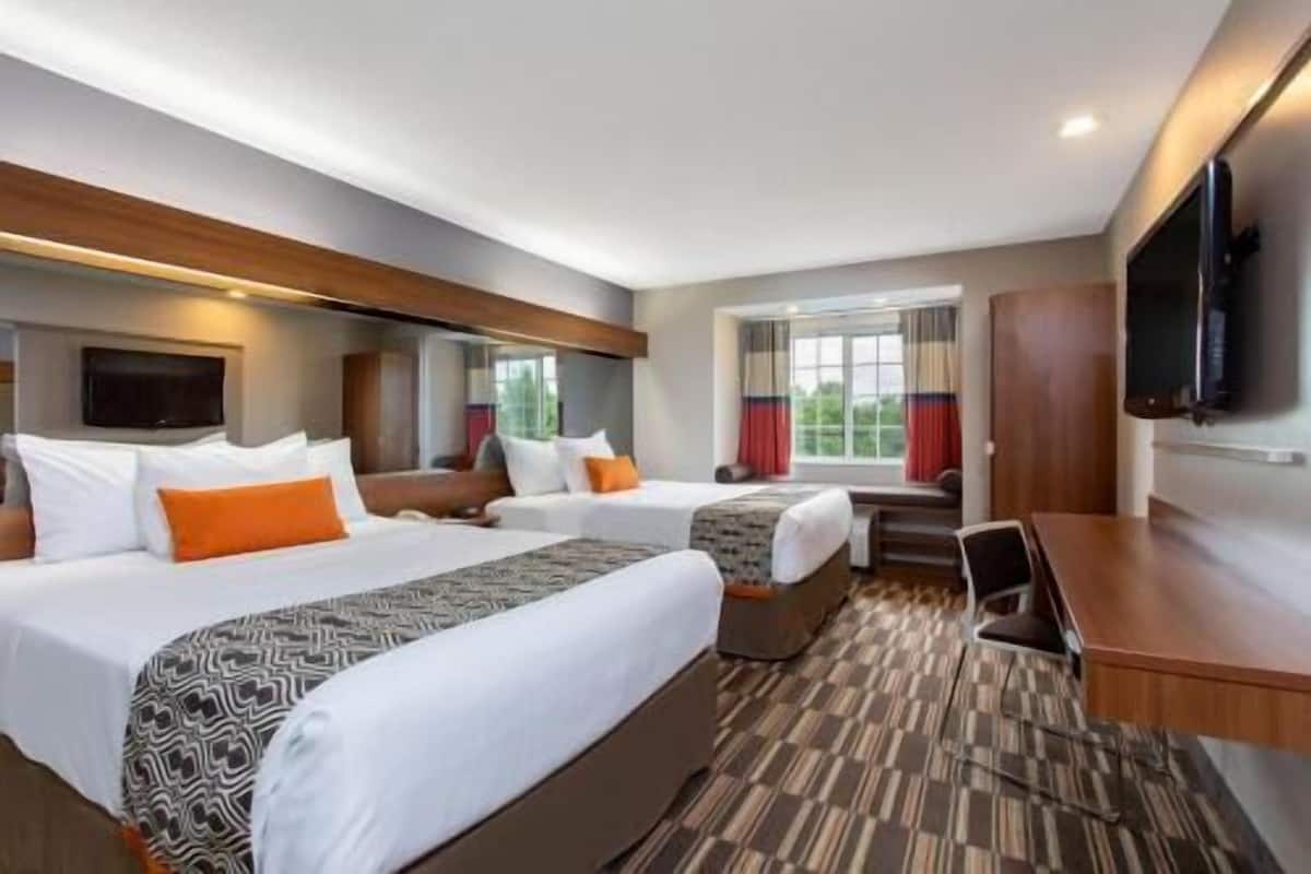 A hotel room with two beds, a desk, a television, and a window with curtains.