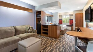 A hotel room with a sofa, a small table, a kitchenette, a TV, and a window with curtains. - Microtel Inn & Suites by Wyndham Philadelphia Airport (Philadelphia)