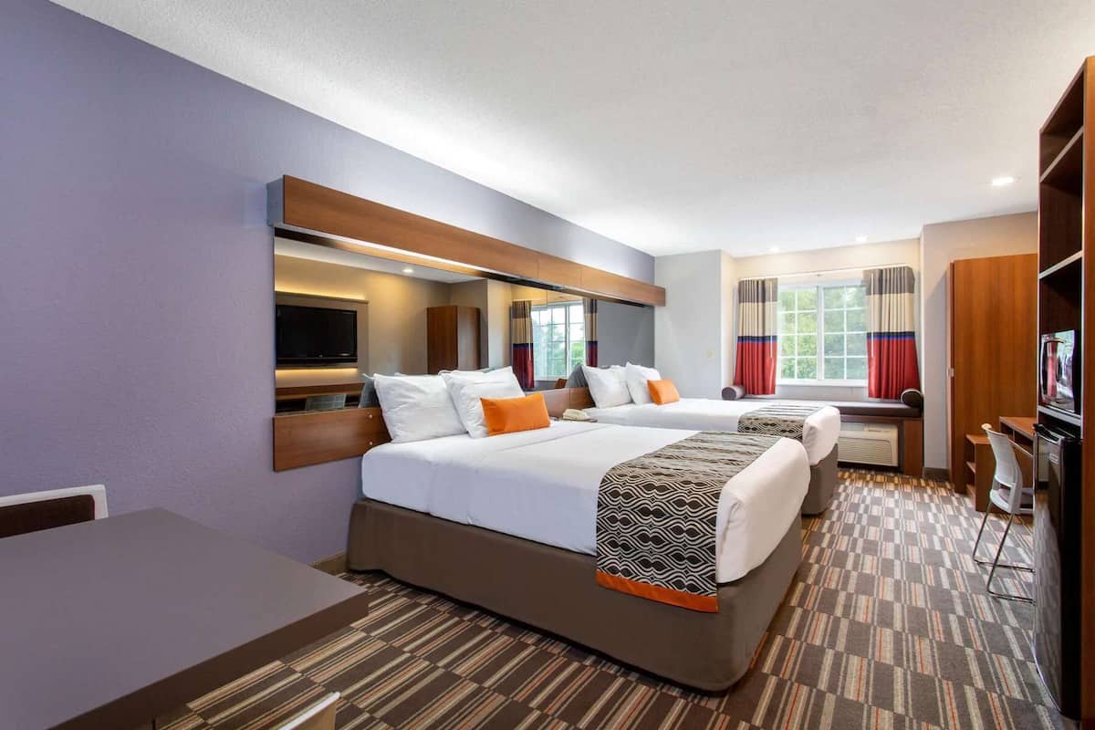 A hotel room with two beds, a TV, a desk, and a large window with curtains.