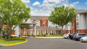 A multi-story hotel with a central entrance, parking area, and surrounding greenery. - Microtel Inn & Suites by Wyndham Philadelphia Airport (Philadelphia)