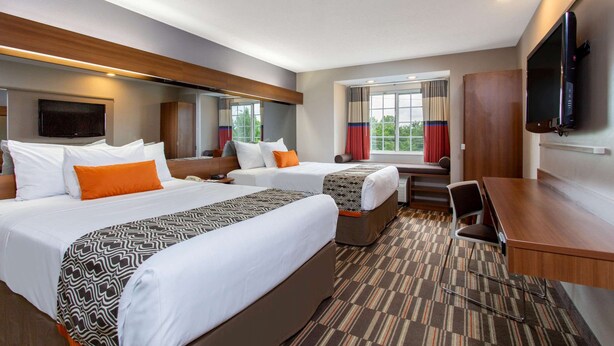 A hotel room with two beds, a desk, a chair, a TV, and a window with curtains. - Microtel Inn & Suites by Wyndham Philadelphia Airport (Philadelphia)