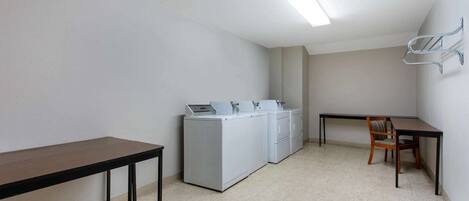 Un cuarto de lavandería con una mesa, una silla y una hilera de lavadoras.