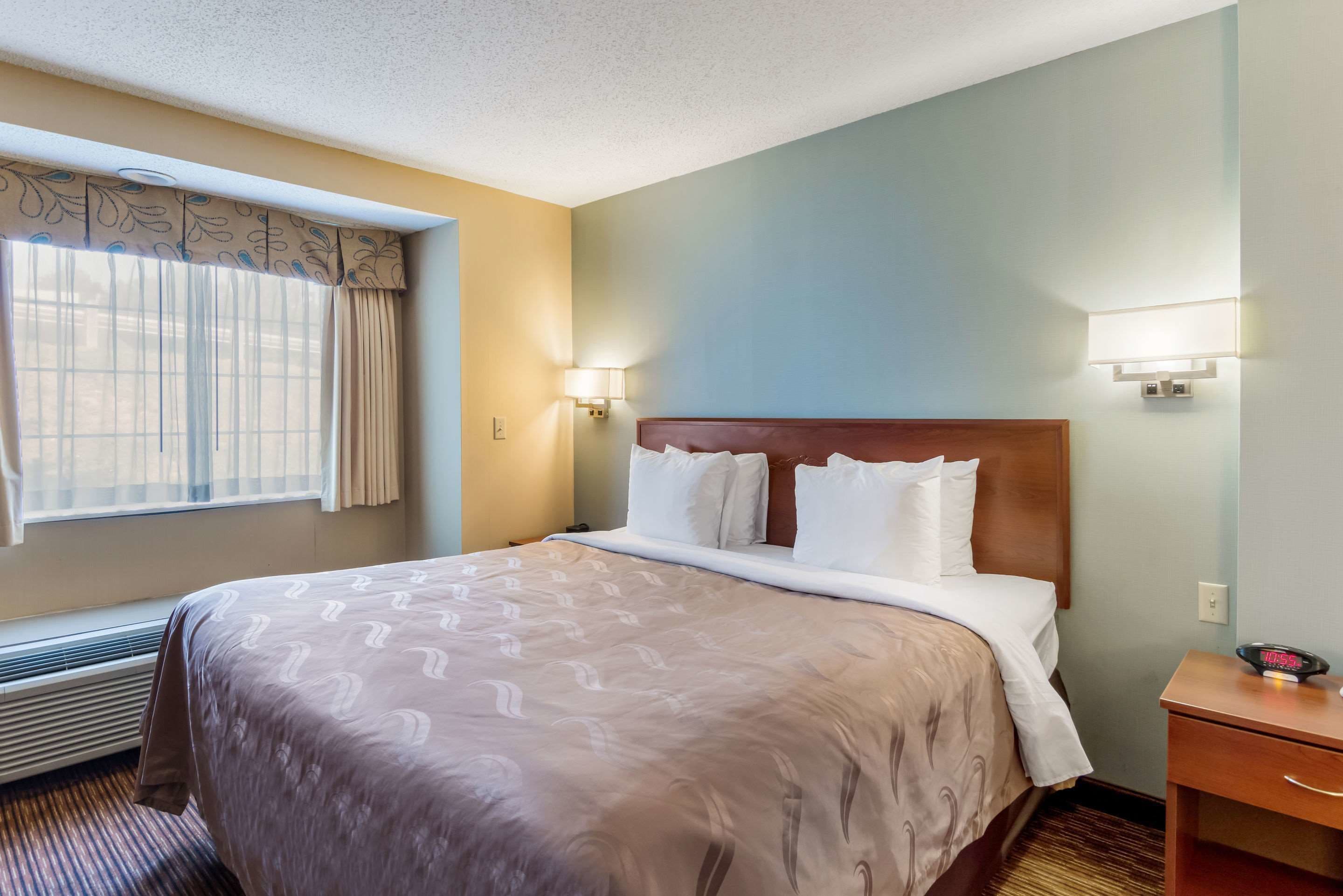 A hotel room with a large bed, two bedside lamps, a nightstand, and a window with curtains.