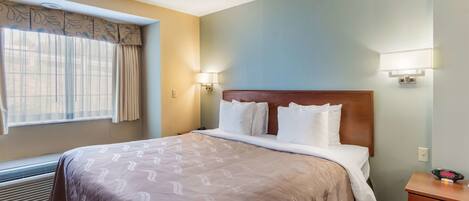 A hotel room with a large bed, two bedside lamps, a nightstand, and a window with curtains.