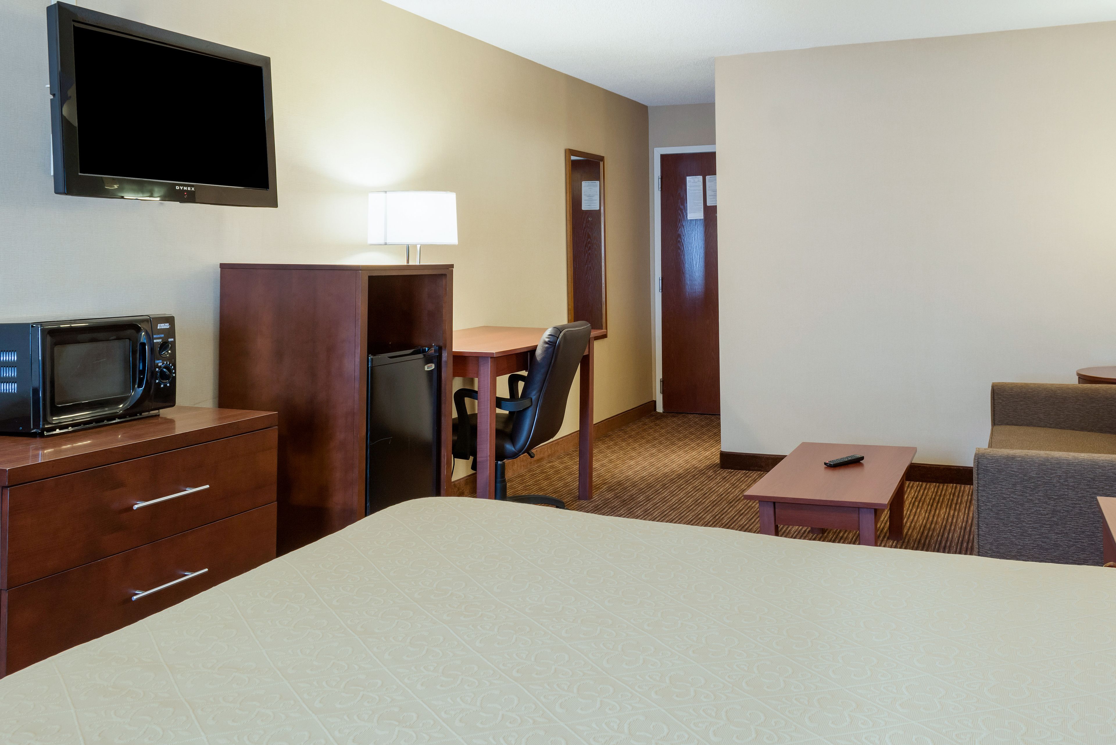 A hotel room with a bed, a desk with a chair, a microwave, a TV, and a small table with a remote control.