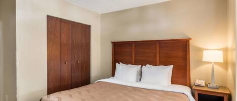 A hotel room with a large bed, a wooden wardrobe, a nightstand with a lamp, and a ceiling light.
