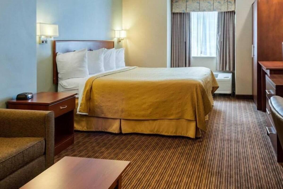 A hotel room with a bed, bedside tables, a desk, a chair, a window with curtains, and a desk lamp.