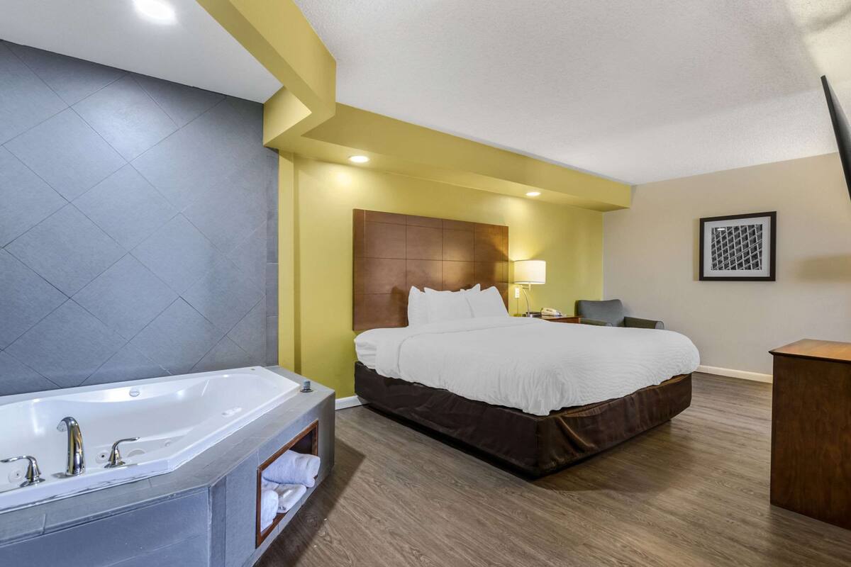 A hotel room with a large bed, a separate bathroom with a bathtub, and a bedside table with a lamp.