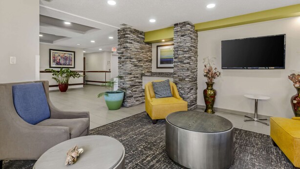 A modern lobby with a stone accent wall, a flat-screen TV, and comfortable seating including a yellow armchair and a grey sofa. - Clarion Pointe Staunton East (Staunton)