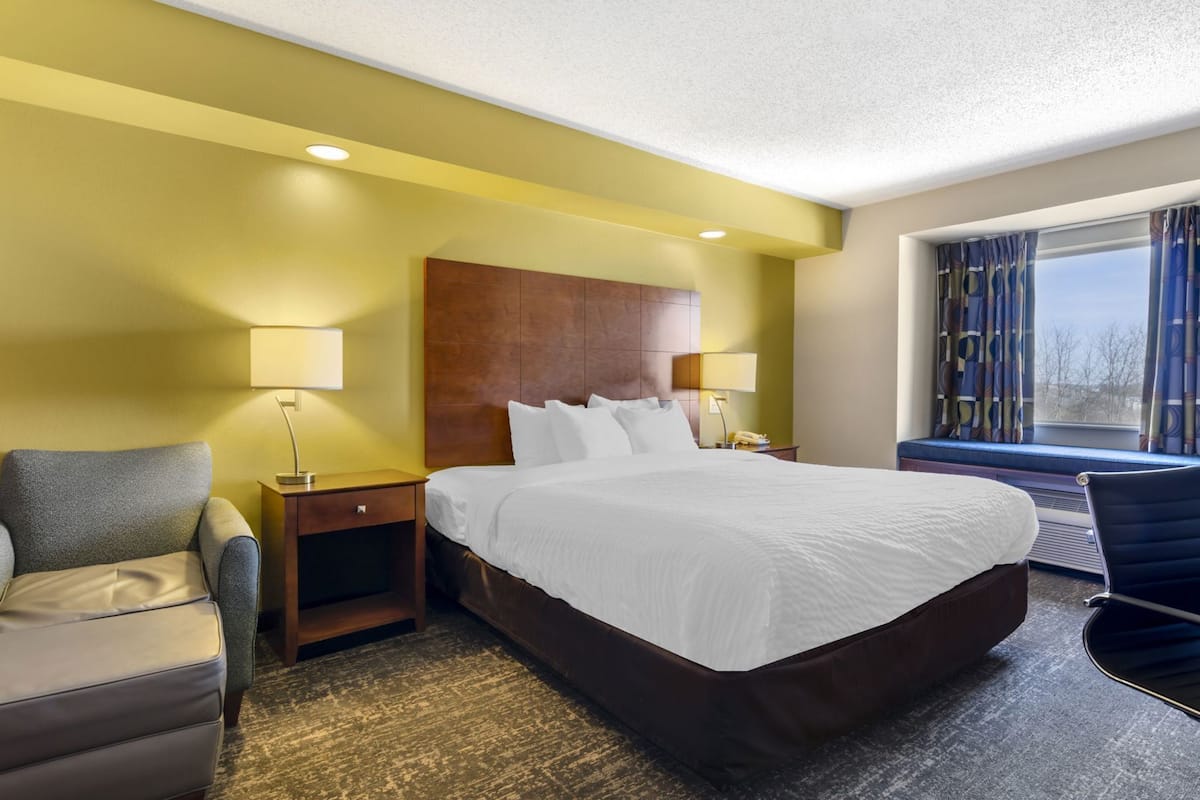 A hotel room with a large bed, two bedside tables with lamps, a chair, and a window with curtains.