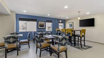 A dining area with tables and chairs, a flat-screen TV mounted on the wall, and framed pictures on the wall.
