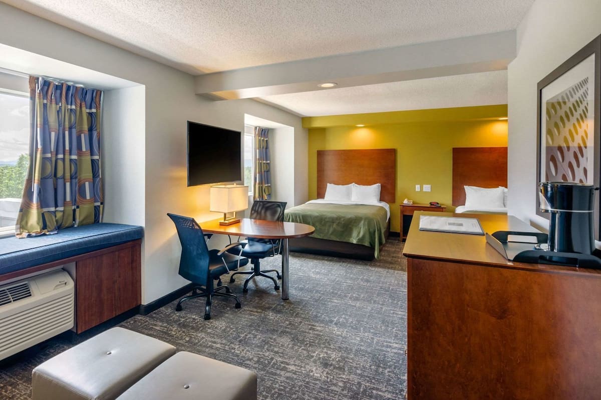A hotel room with a bed, desk, chair, and a small table.