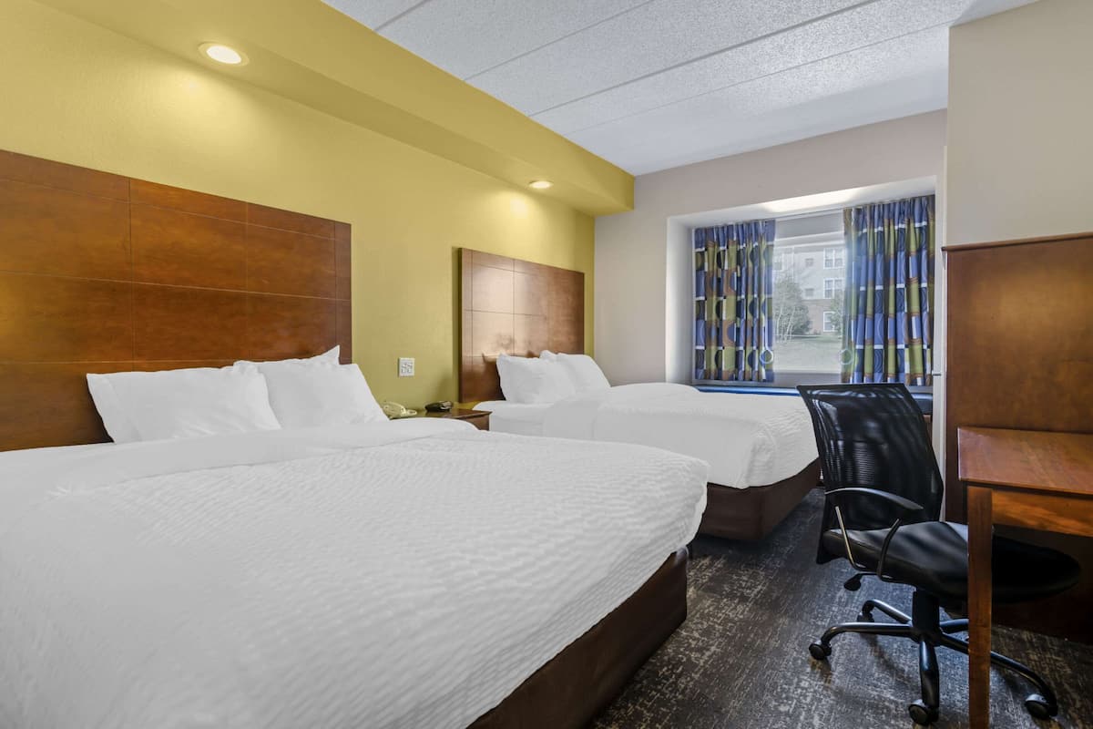 A hotel room with two beds, a desk, and a chair.