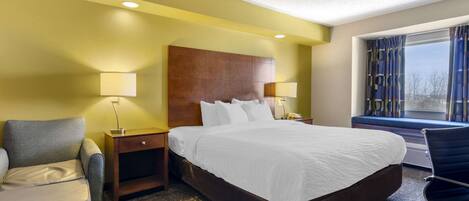 A hotel room with a large bed, two bedside tables with lamps, a chair, and a window with curtains.