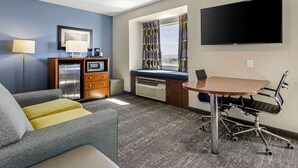 A hotel room with a sofa, a small desk with a chair, a flat-screen TV, a microwave, and a mini-fridge. - Clarion Pointe Staunton East (Staunton)