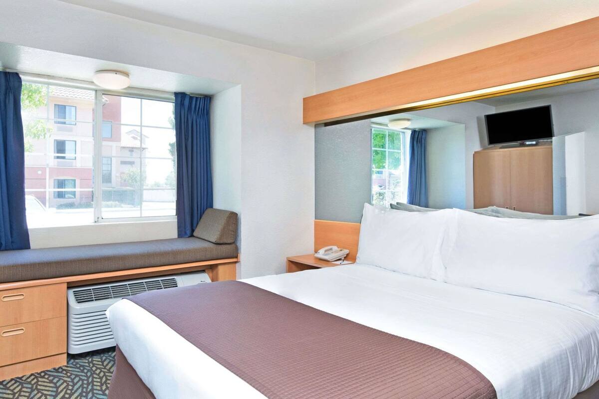 Une chambre d’hôtel comprenant un lit, un bureau avec une chaise, un téléphone et un téléviseur.
