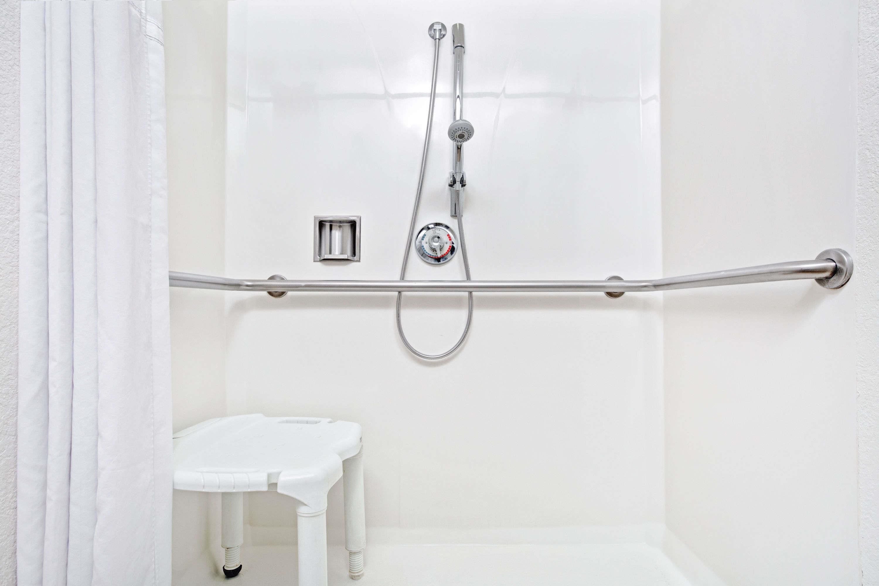 A white bathroom with a shower, grab bar, and a small white toilet.