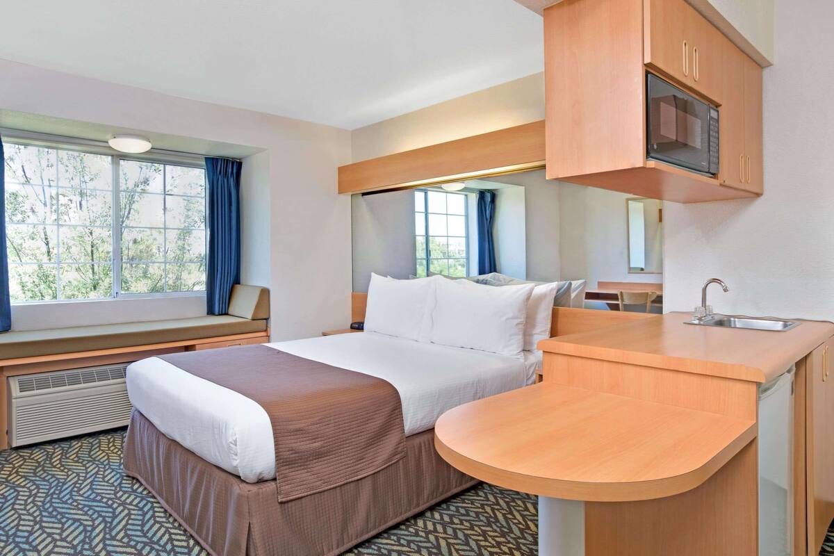 Une chambre d’hôtel équipée d’un lit, d’un bureau intégré, d’un four à micro-ondes et d’une fenêtre avec des rideaux.