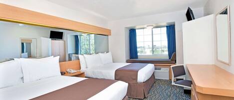 A hotel room with two beds, a desk, a chair, a TV, and a window with curtains.