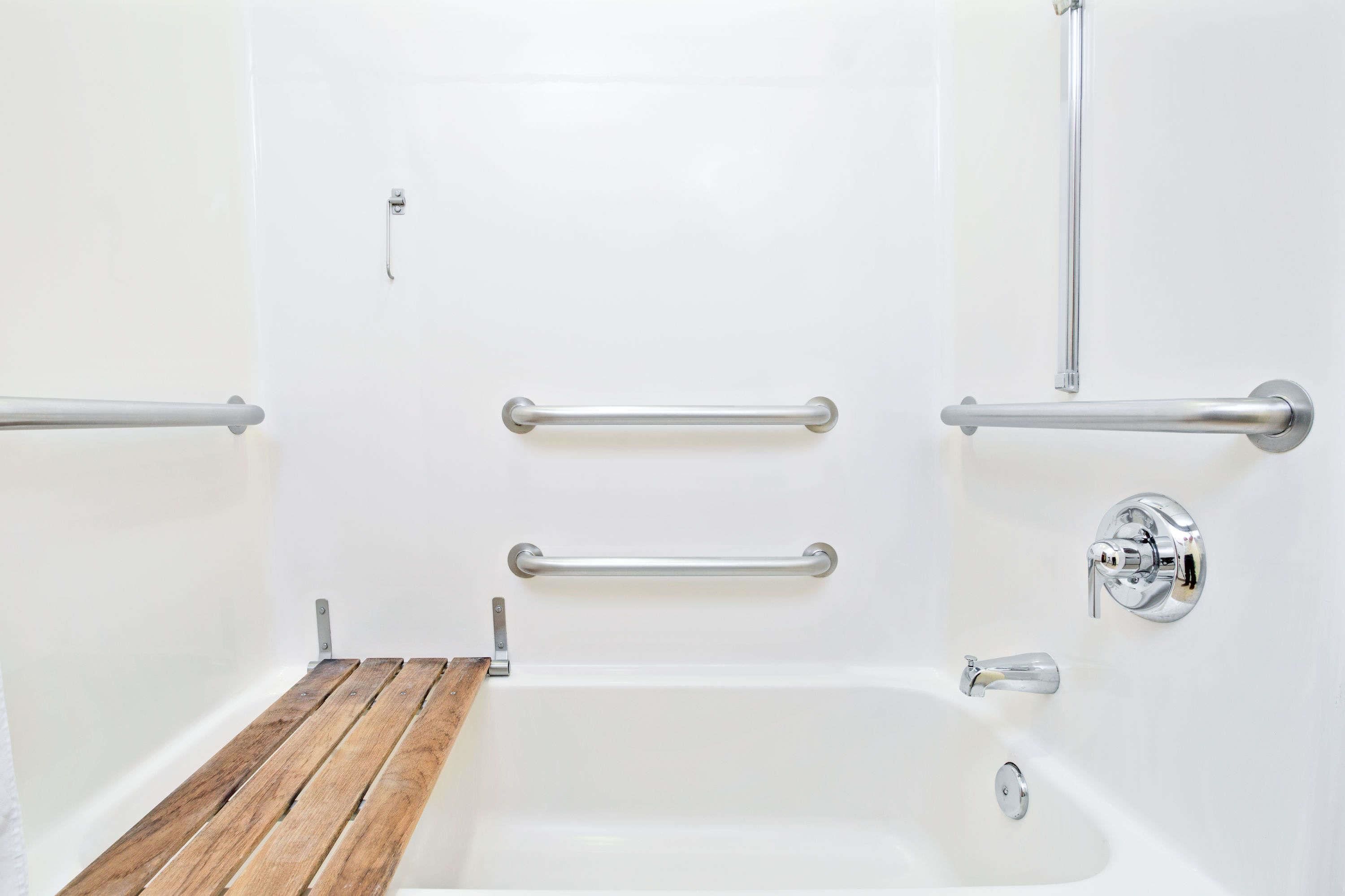A white bathtub with chrome fixtures, wooden bench, and grab bars.