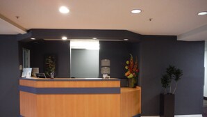 A reception desk with a blue and wooden design, a mirror above it, and a potted plant to the right. - Microtel Inn & Suites by Wyndham Morgan Hill/San Jose Area (Morgan Hill)