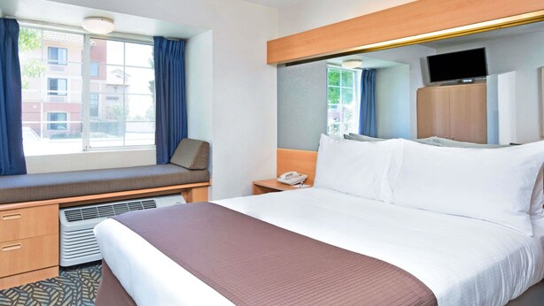 A hotel room with a large bed, a window seat, a television, and a desk with a phone. - Microtel Inn & Suites by Wyndham Morgan Hill/San Jose Area (Morgan Hill)