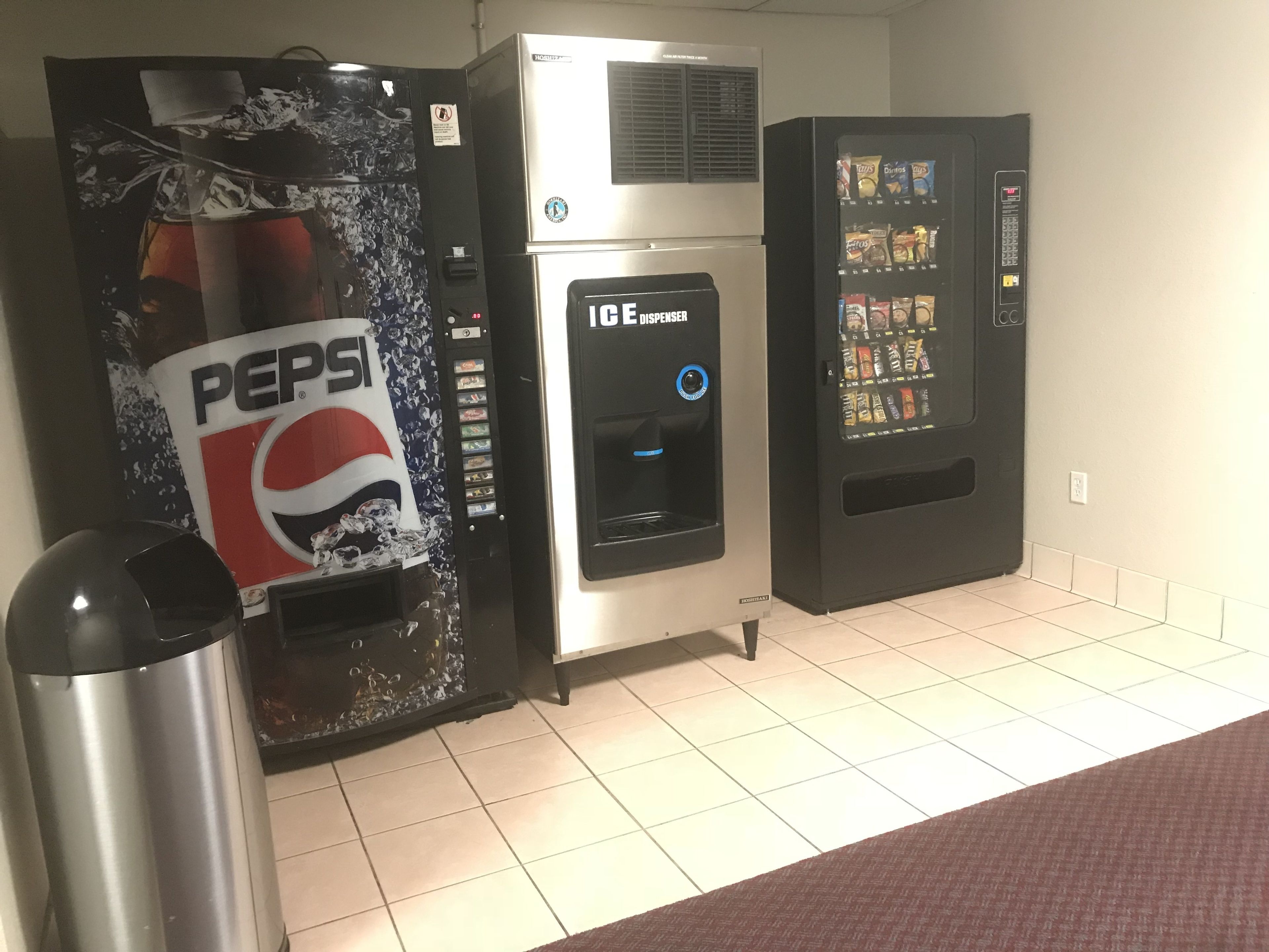 Espaço com máquinas de venda automática, incluindo um dispensador de Pepsi, um dispensador de água e uma máquina de lanches.
